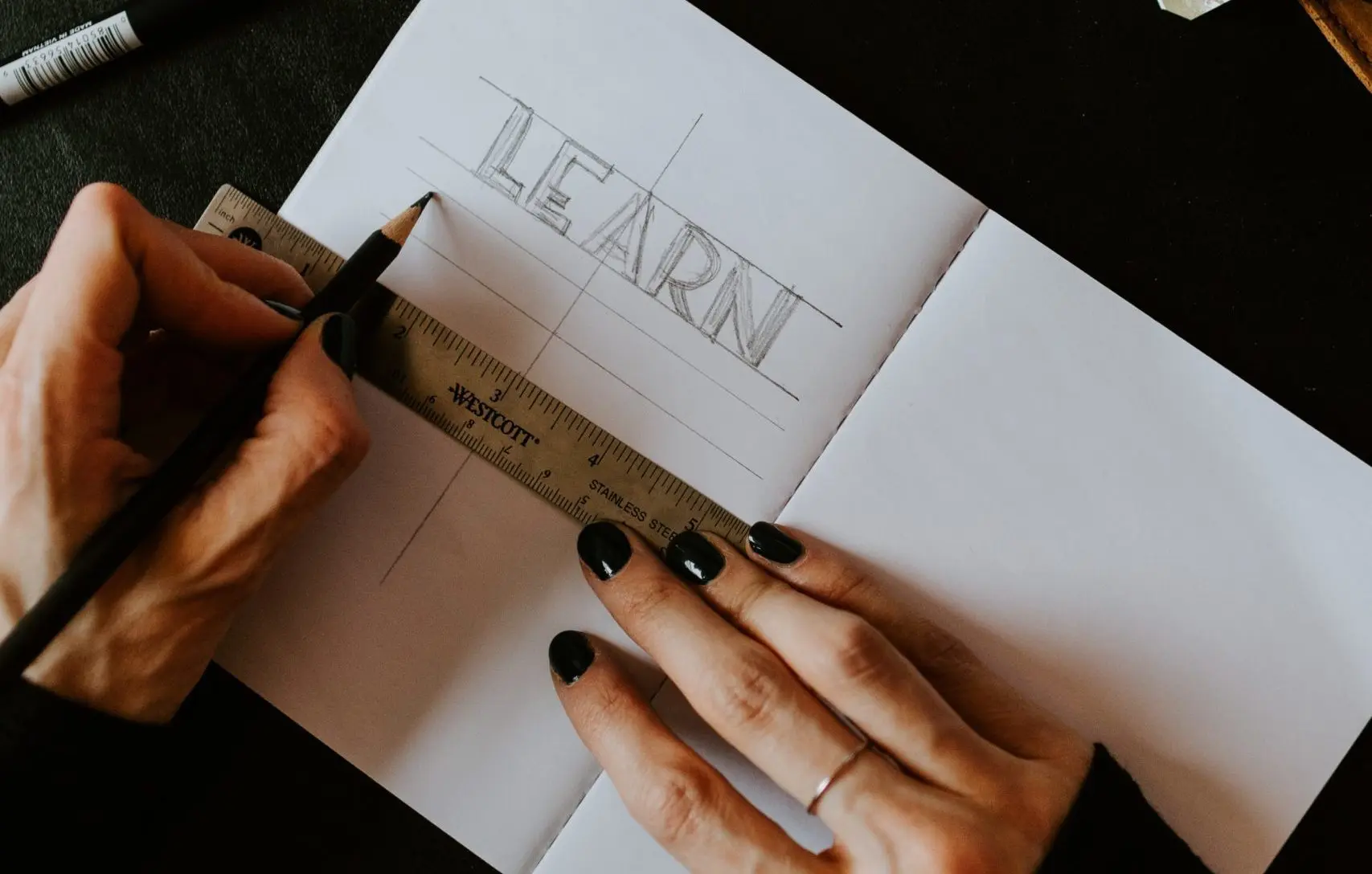 Mujer escribiendo en un cuaderno la palabra learn con una regla y un lápiz
